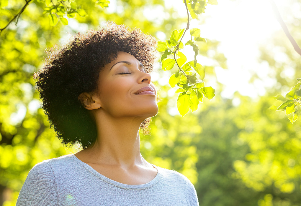 person standing in nature with tree branch inhaling with eyes closed
