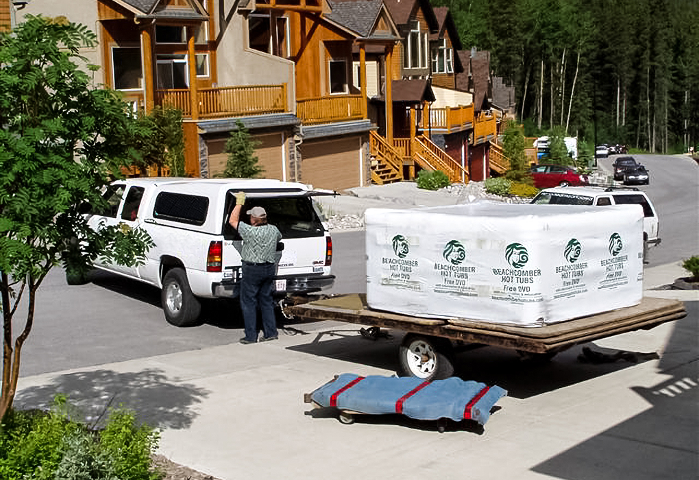 white truck with trailer holding wrapped beachcomber hot tub outside a home