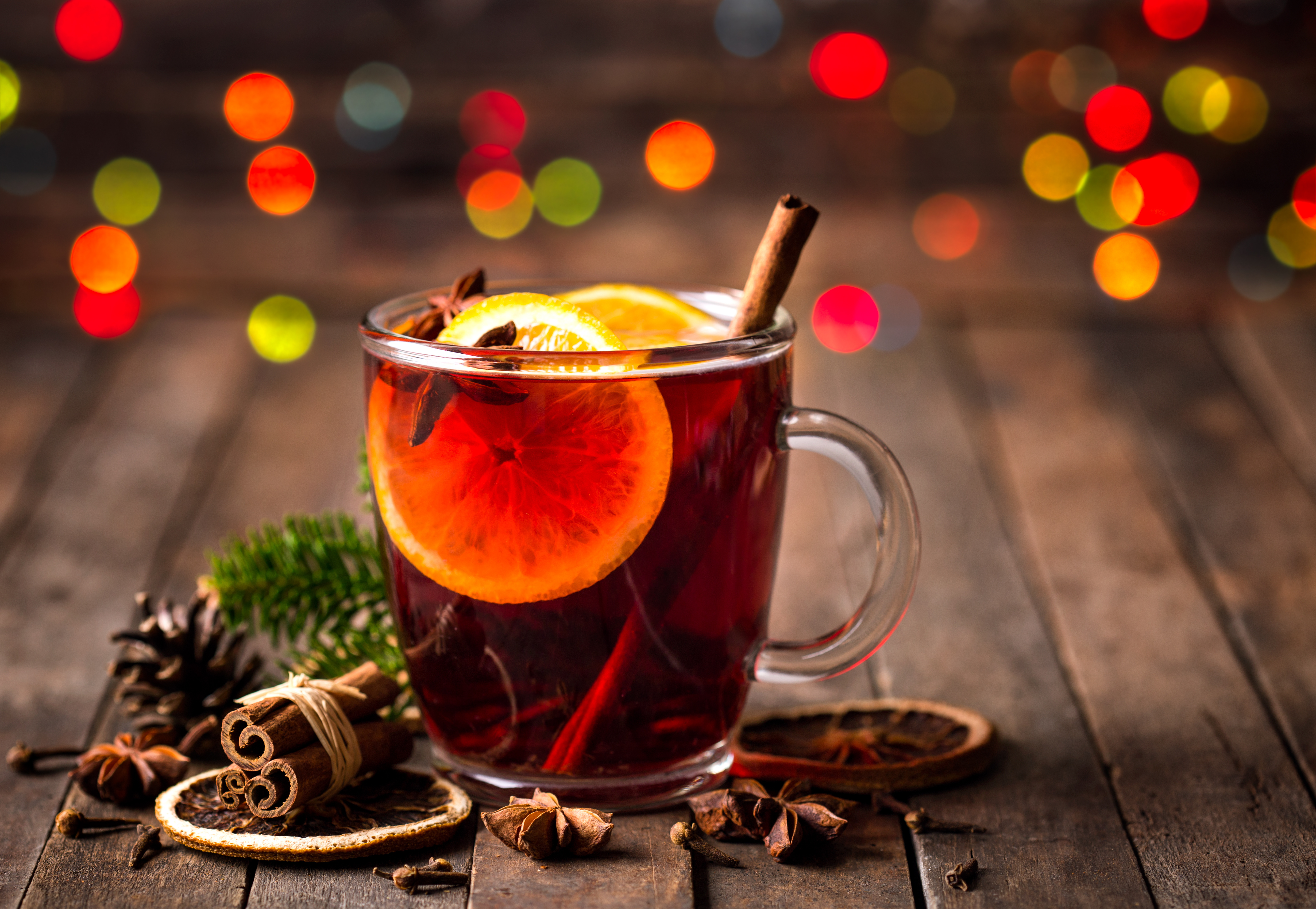 mulled wine in a glass cup with orange slice and dried acorns around it and colourful lights blurred in the background