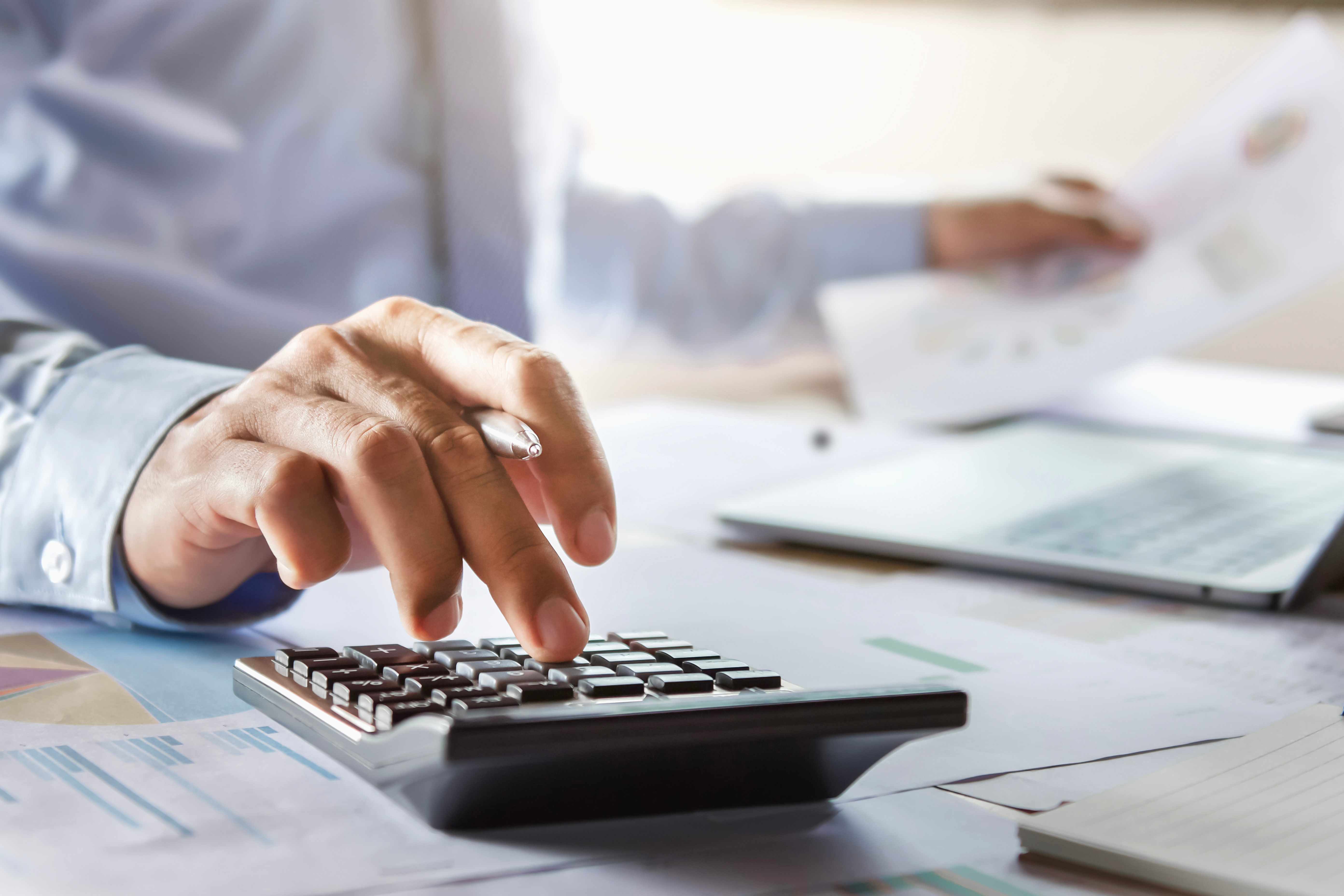 blurred background with focus on a calculator on desk and man using it while holding sheets