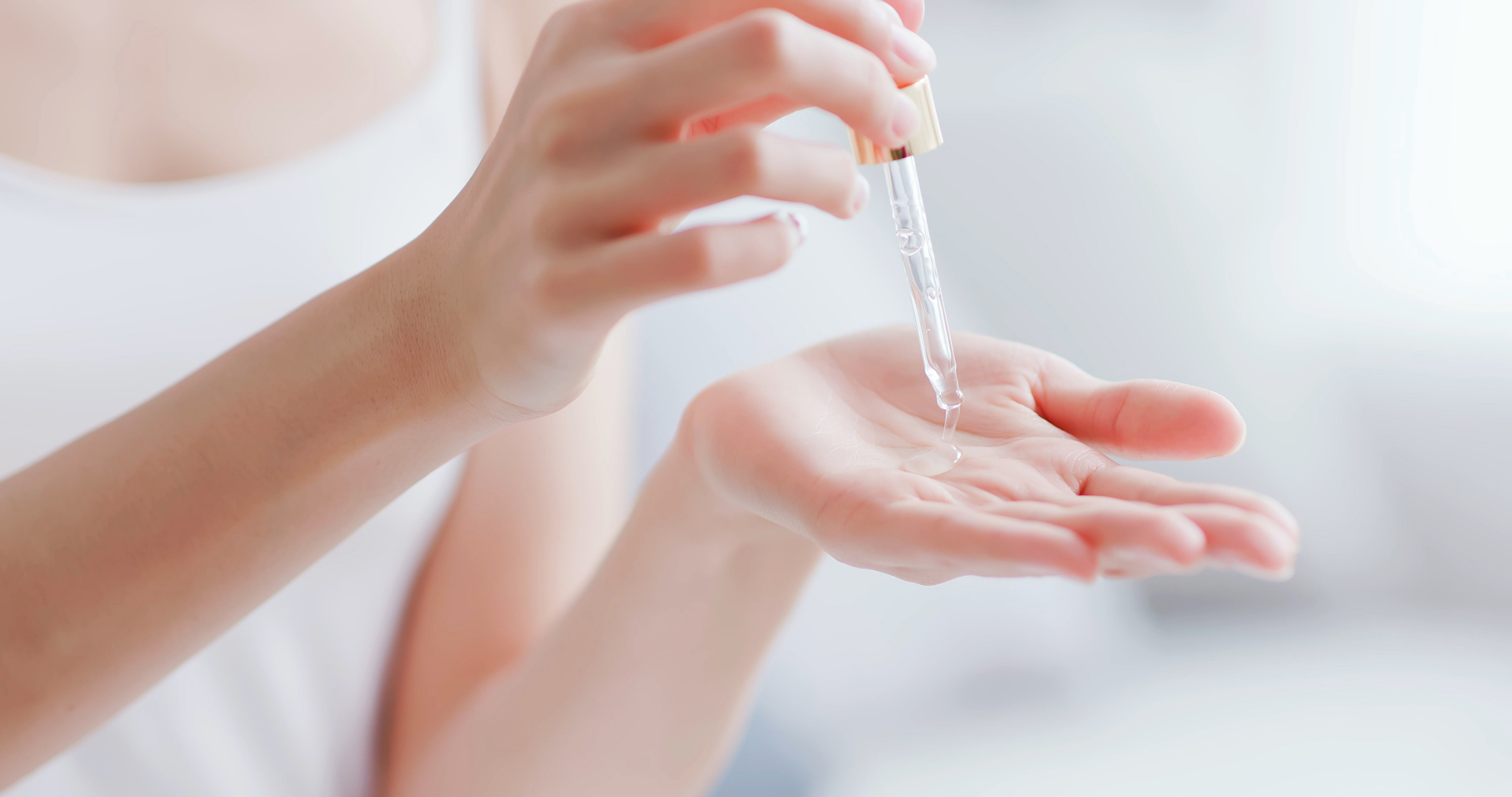 woman's hands with a pipette of serum, squeezing the pipette so the serum falls onto her hand