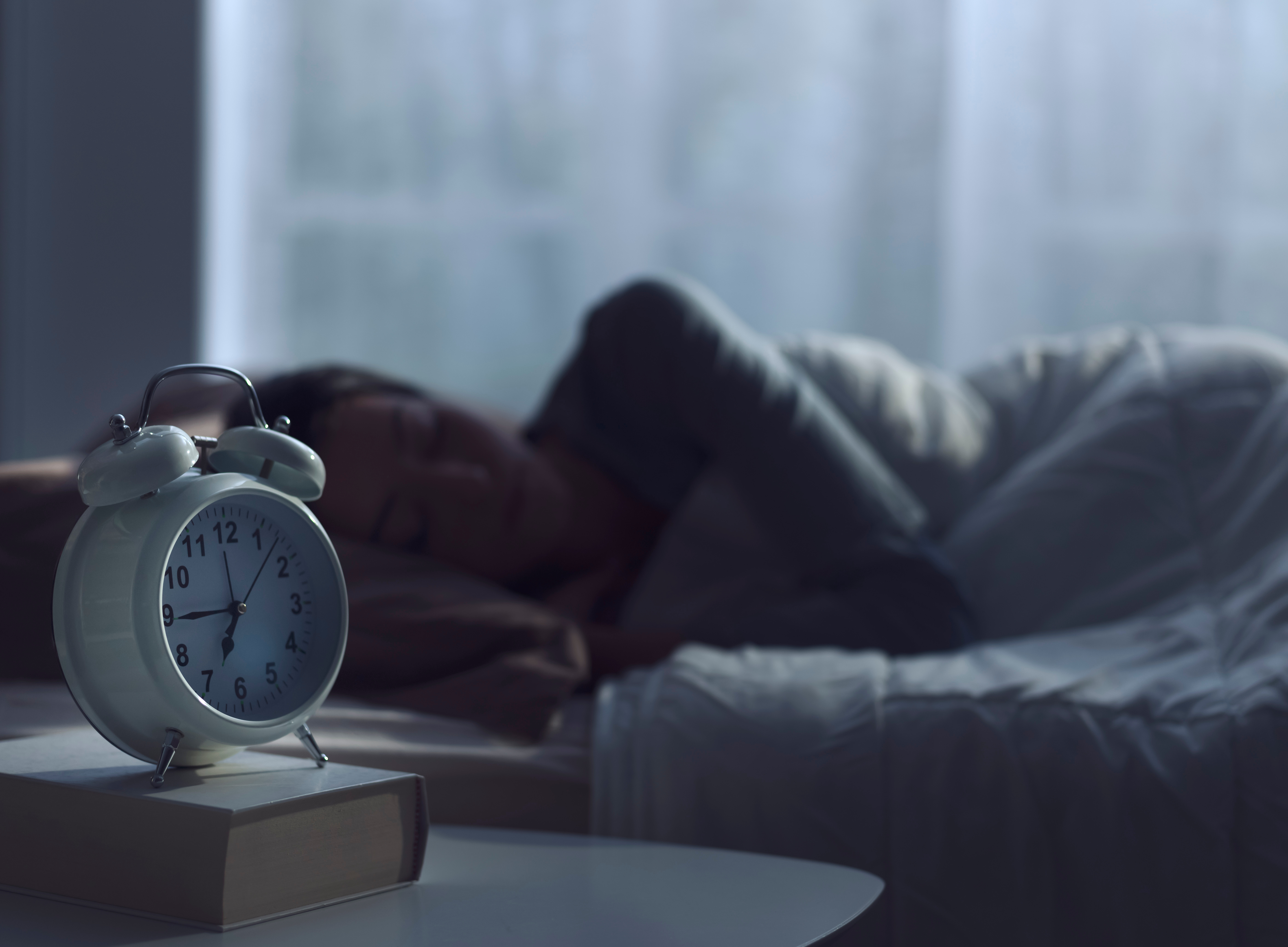 dark room, someone sleeping in bed, alarm clock on the side table