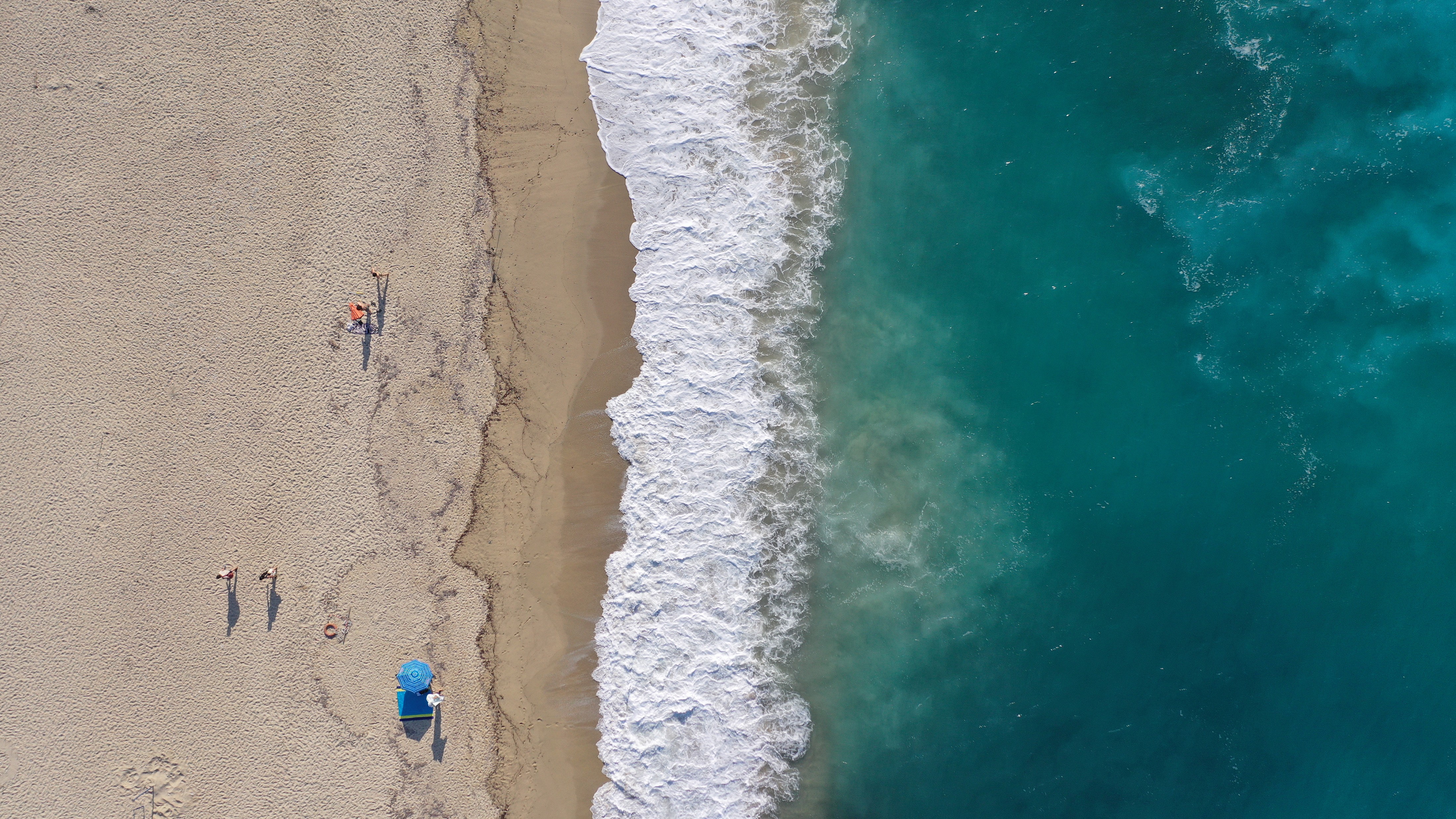 aerial view of sandy beach with people and parasol umbrella alongside turquoise shore