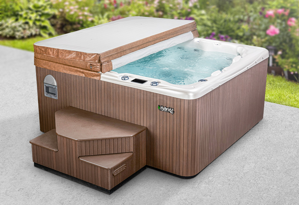beachcomber hybrid4 hot tub on stone patio with flower bushes in the background