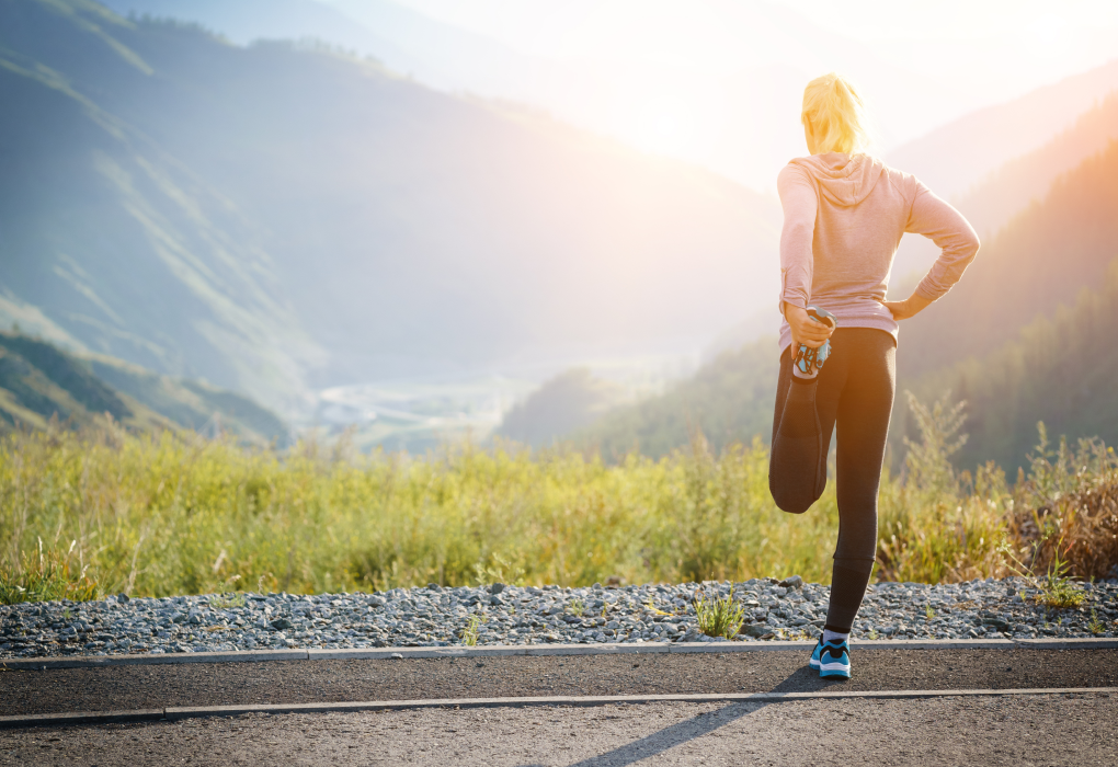 a woman on a path staring toward mountains and stretchin her quad muscle