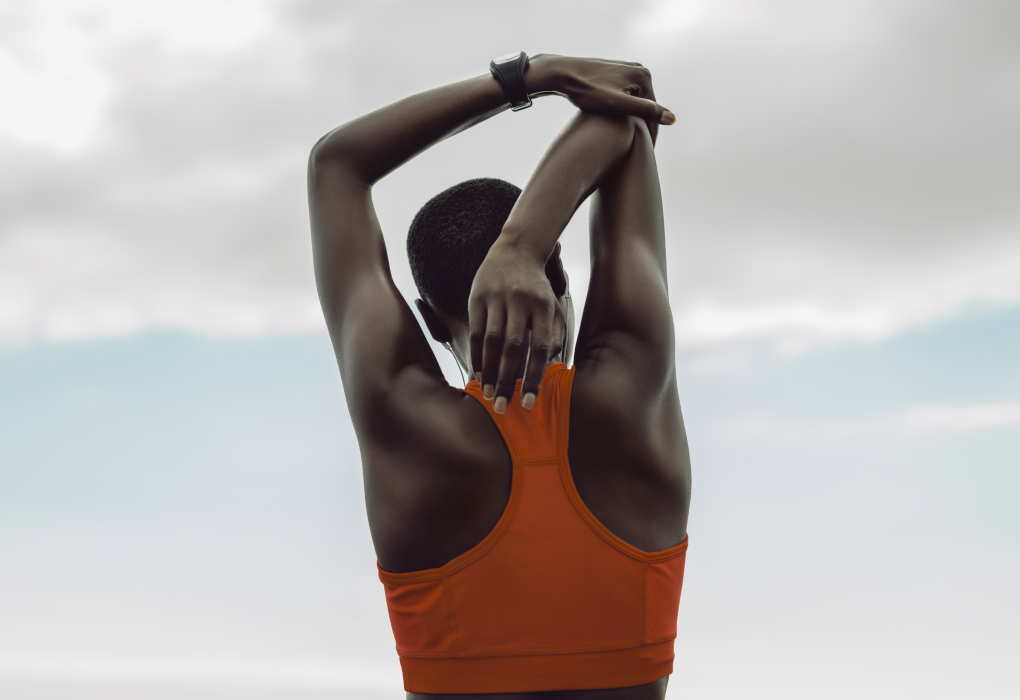 woman with back turned to camera stretching with her arm above her head