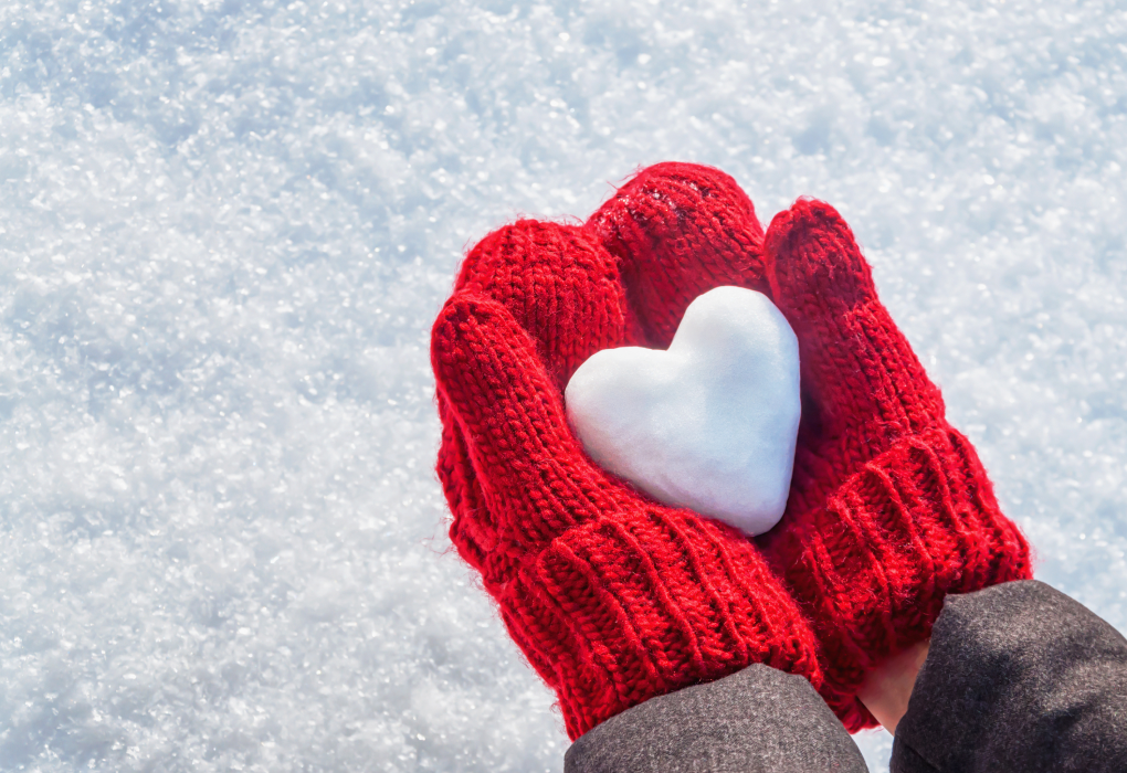 red gloved hands holding a heart made out of snow