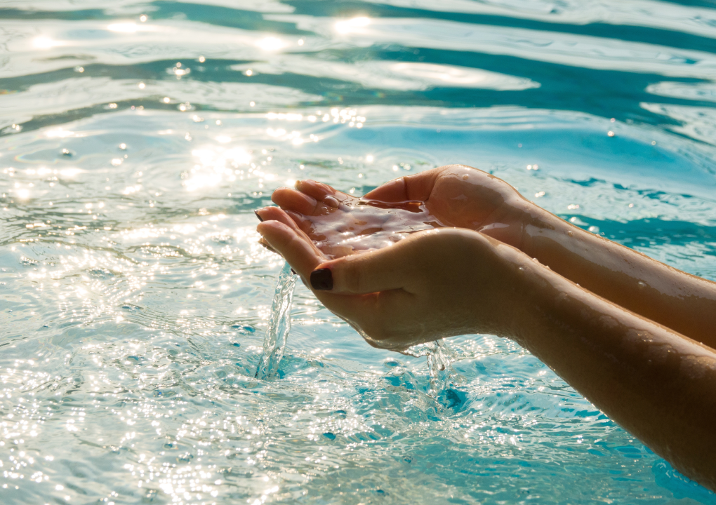 hands cupping water over a body of water