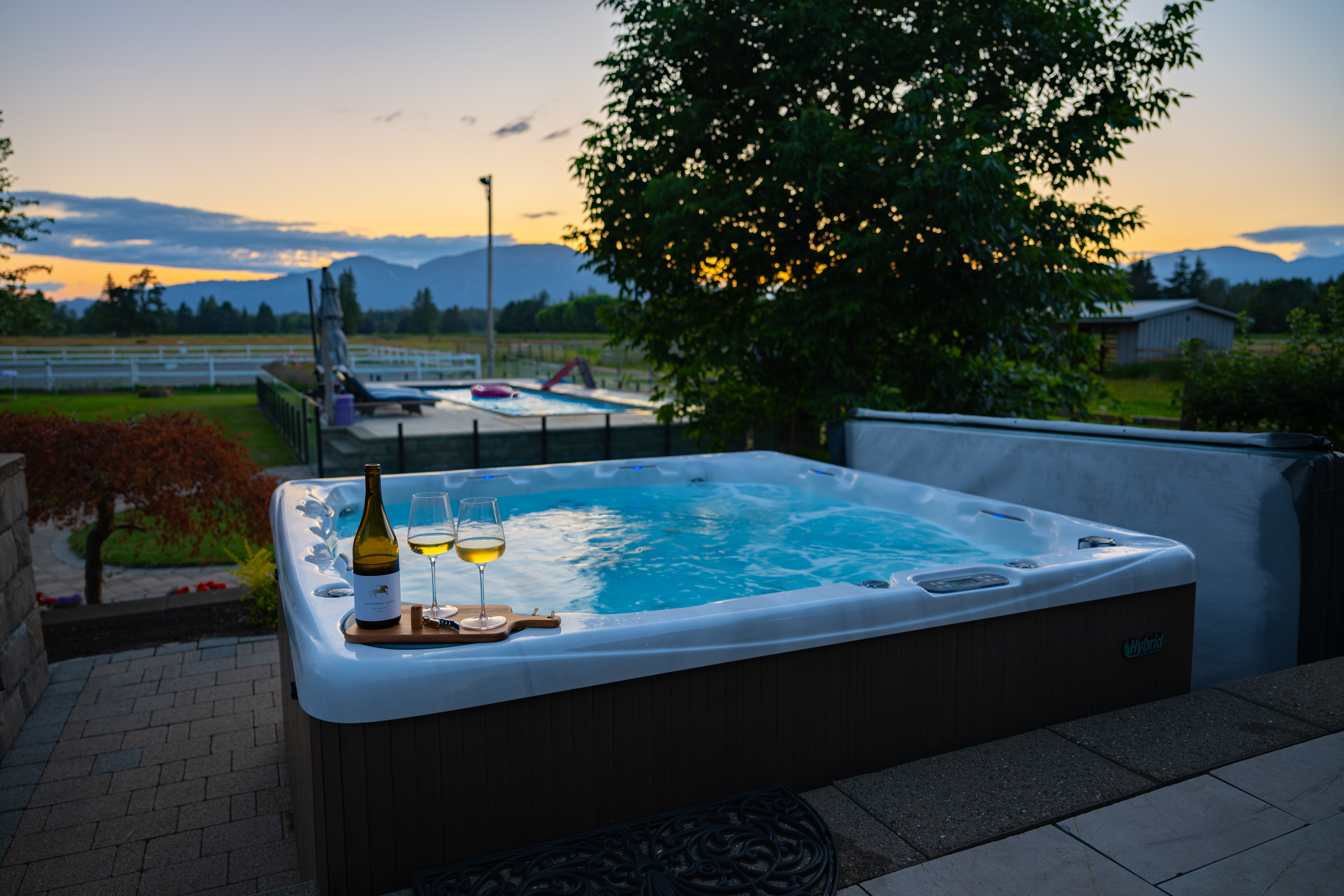 hot tub in a backyard with mountains and sunset in the background. bottle of wine and wine glasses sitting on the hot tub